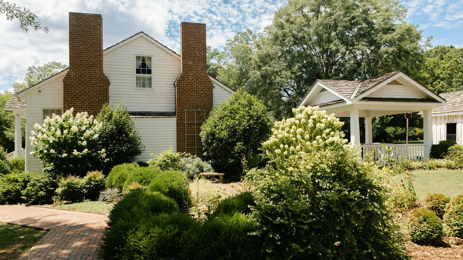 White home with two brick chimneys, surrounded by shrubs and bushes