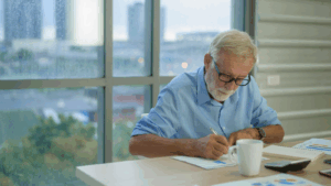 Senior man writing at a desk with a coffee cup nearby