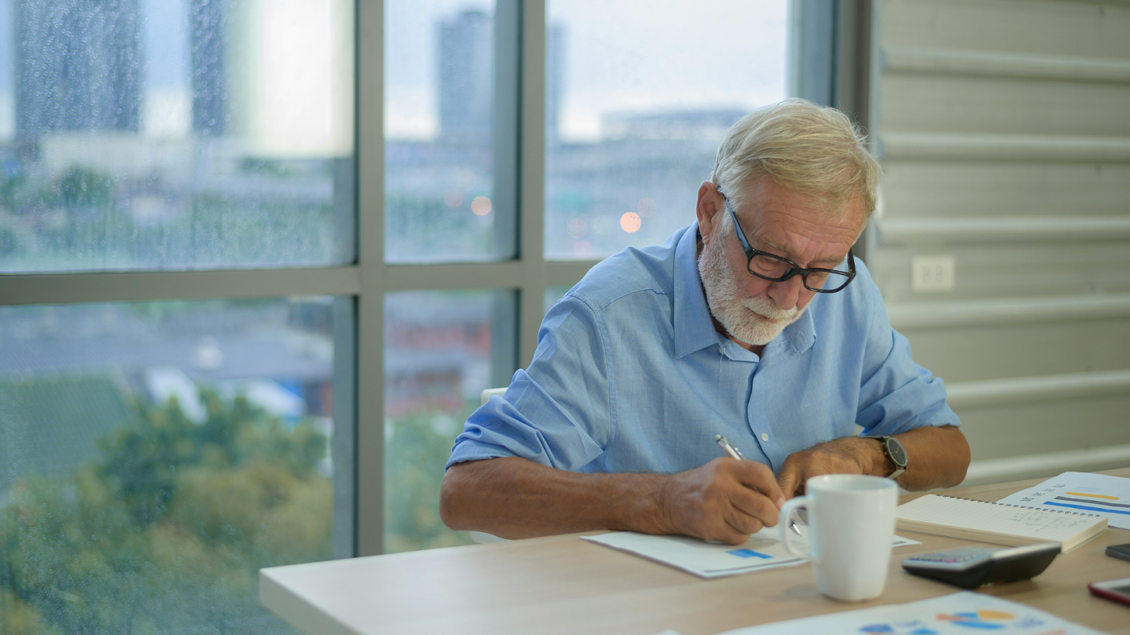 Senior man writing at a desk with a coffee cup nearby