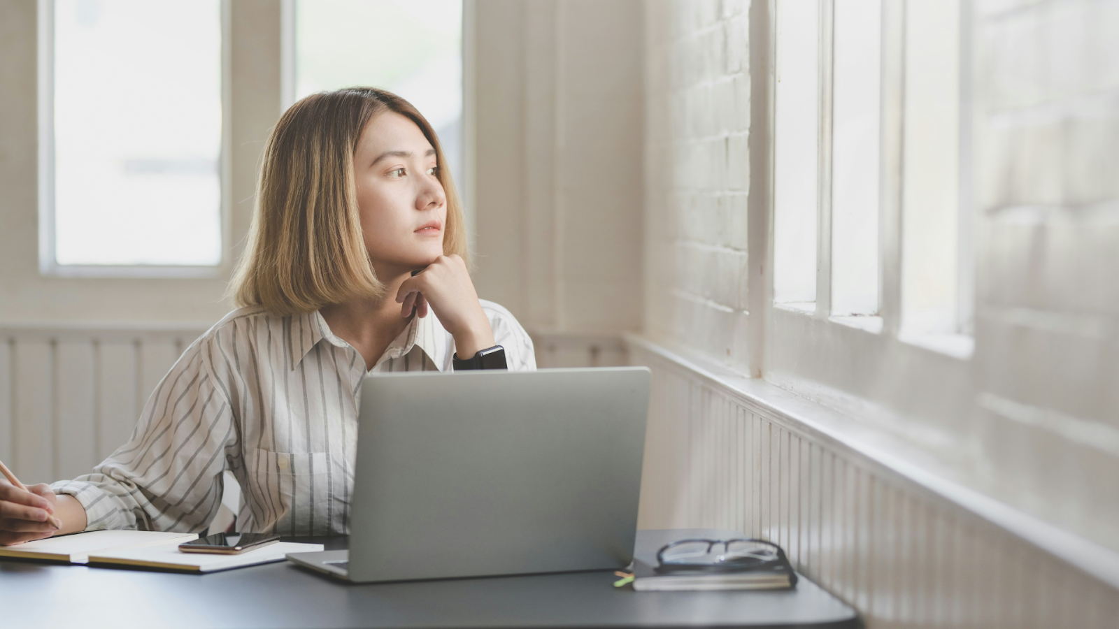 Woman peering out a window and writing on a notepad